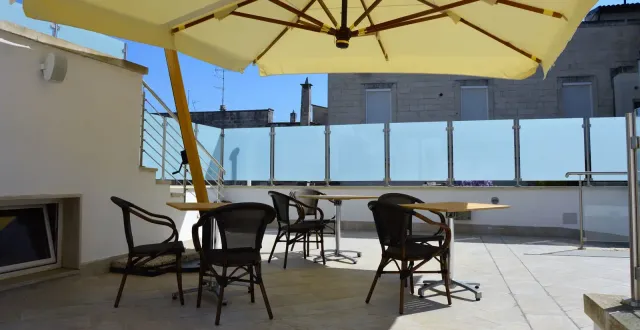 Outdoor patio with tables, chairs, and large umbrella, with buildings visible in the background.