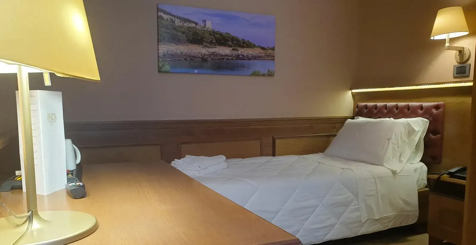Camera d'albergo con letto, scrivania con lampada e quadri paesaggistici alla parete.
