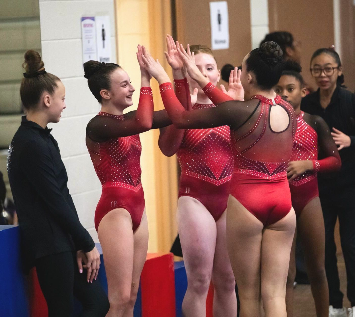 A group of girls in red leotards are giving each other high fives