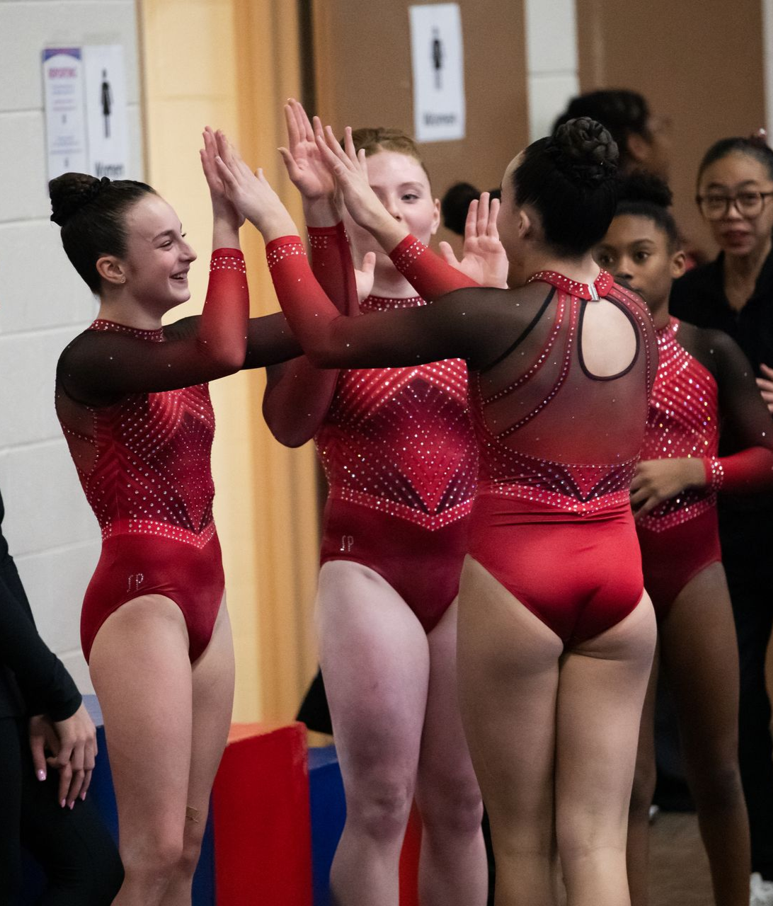 A group of girls in red leotards are giving each other high fives