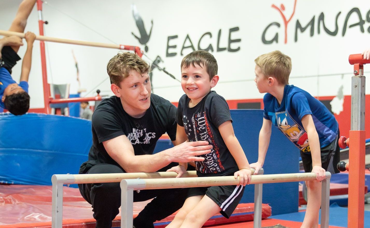 A man is helping a young boy on a bar in a gym.