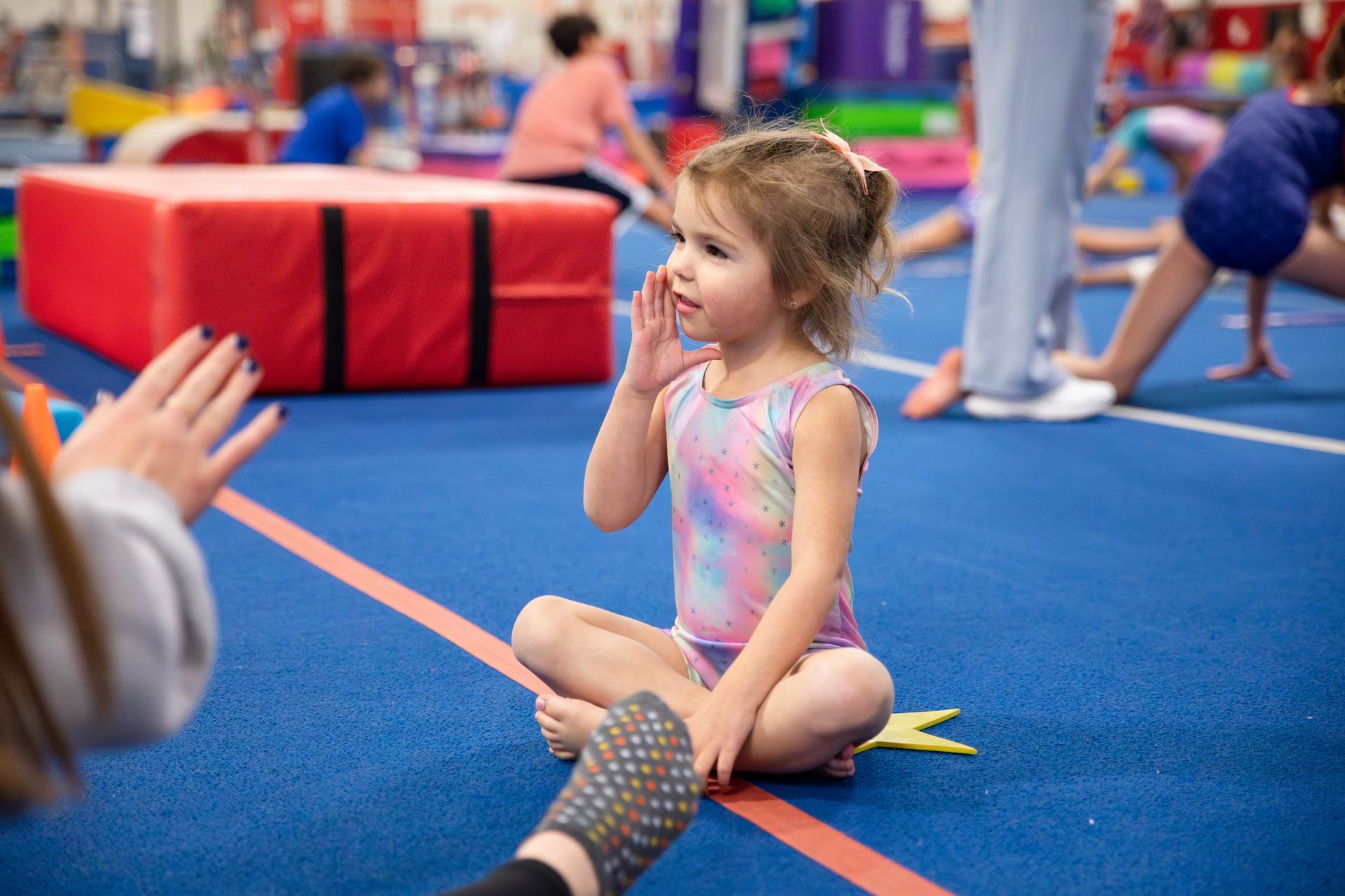 A woman with a tattoo on her arm is helping a little girl balance on a balance beam