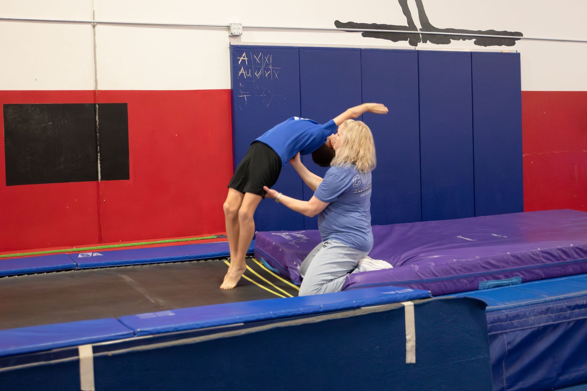Two female gymnasts are laughing together while standing next to each other in a gym.