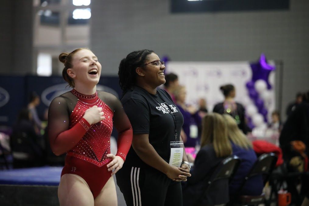 Two female gymnasts are laughing while standing next to each other in a gym.