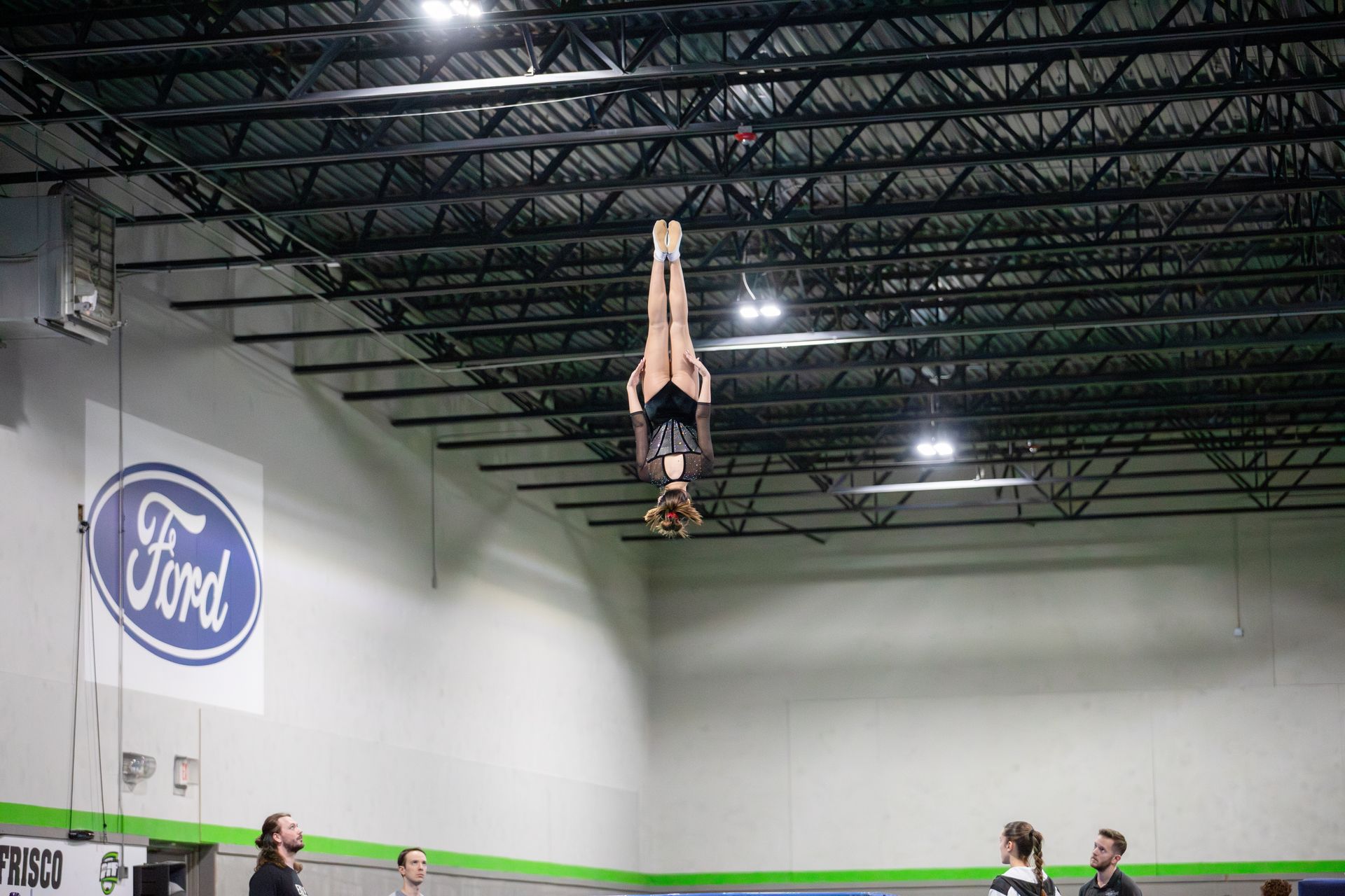 A woman is doing a handstand in a gym in front of a ford sign.