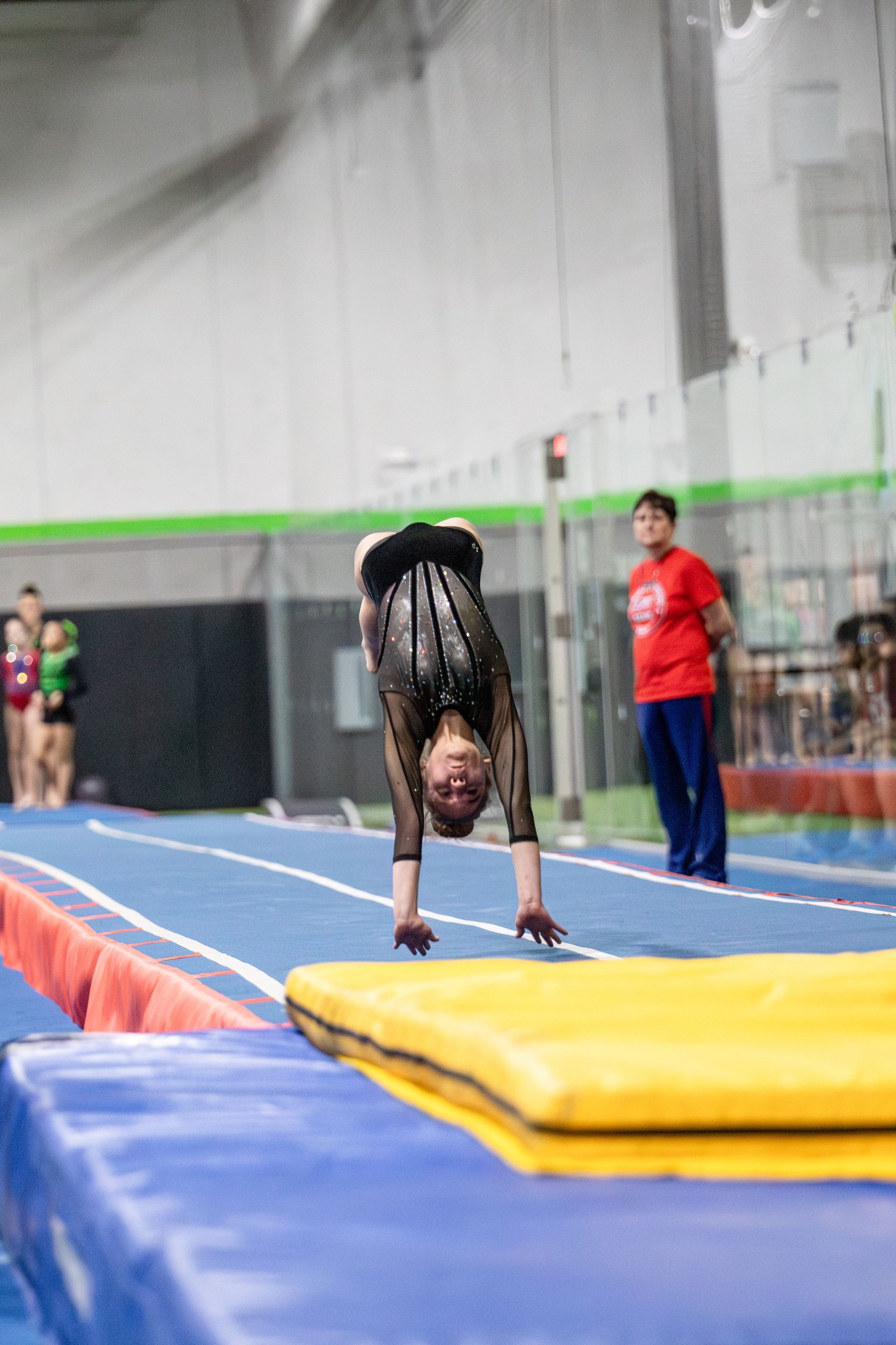 A young girl is doing a handstand on a mat in a gym.