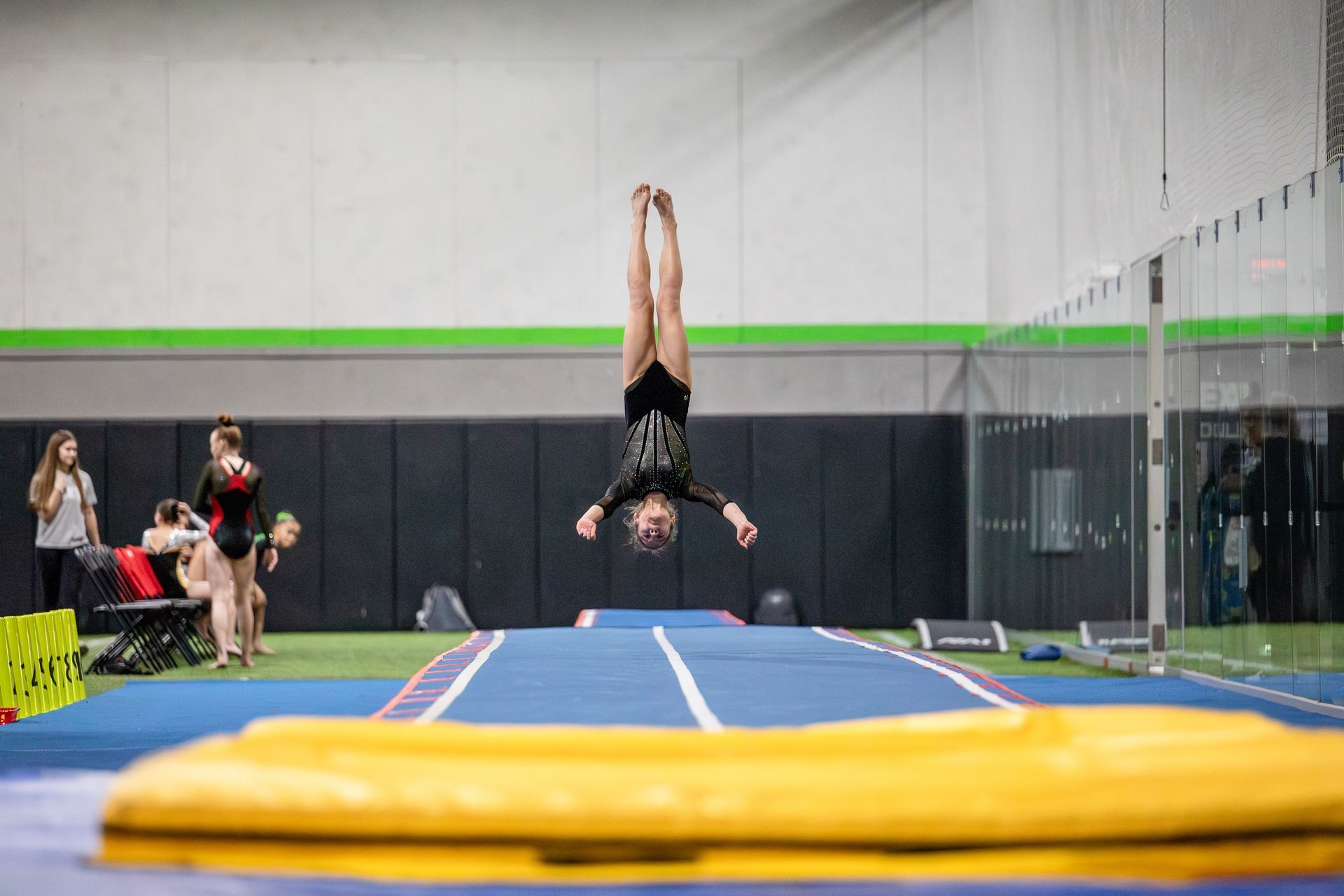 A girl is doing a handstand on a trampoline in a gym.