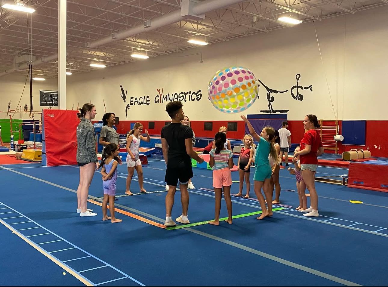 A group of children are playing with a colorful parachute in a gym.