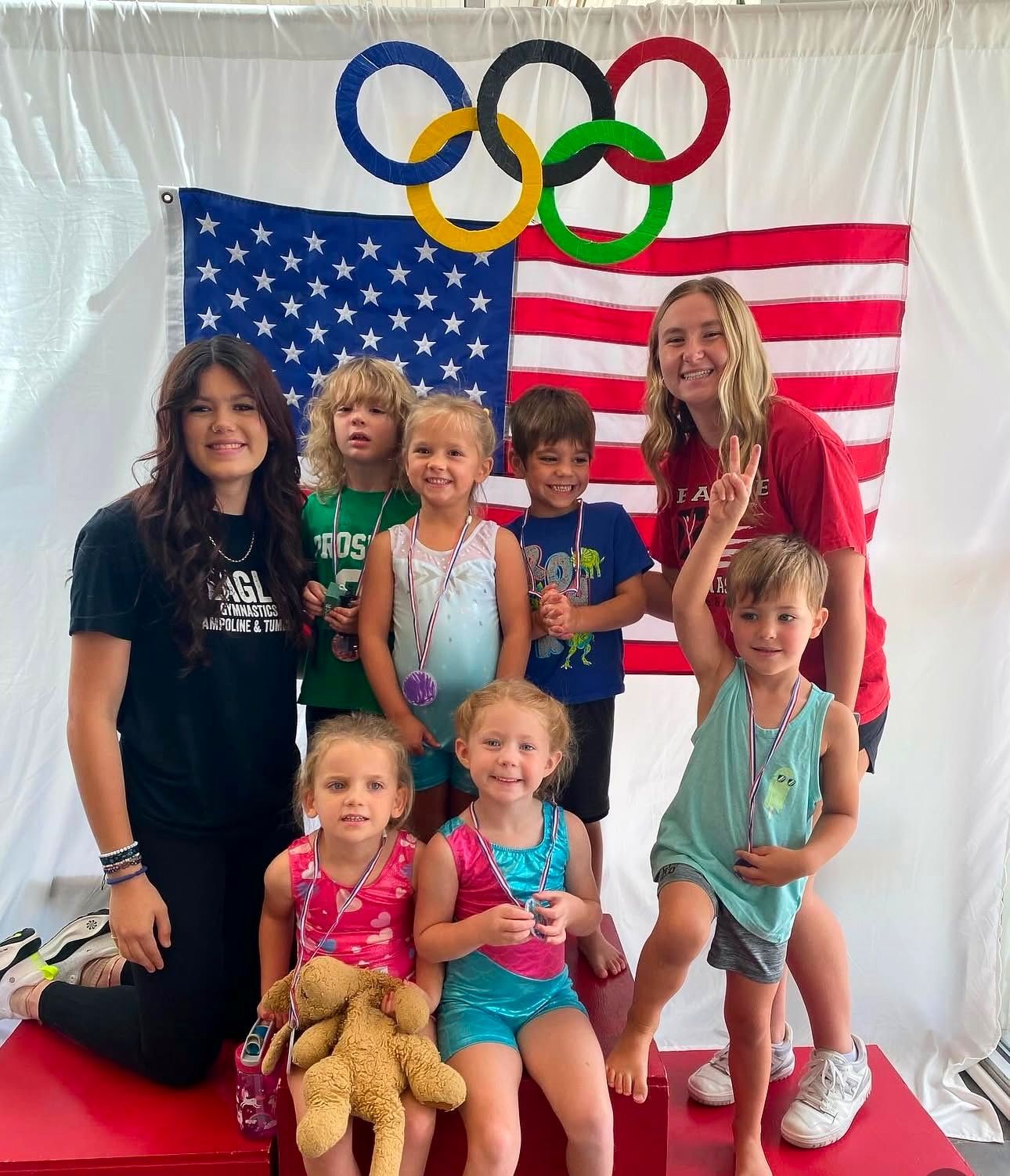 A group of children are posing for a picture in front of an american flag and olympic rings.