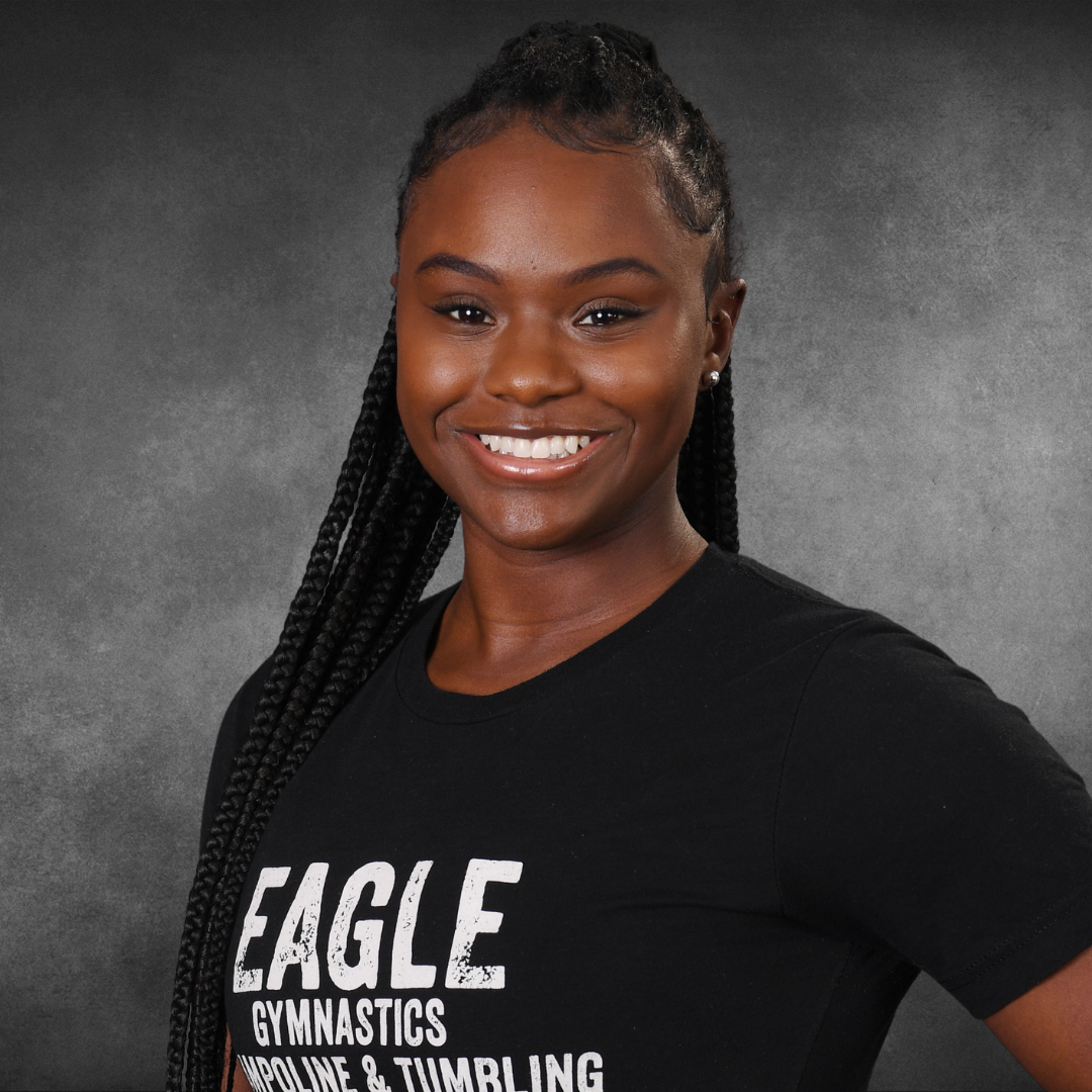 A woman wearing a black eagle gymnastics shirt smiles for the camera