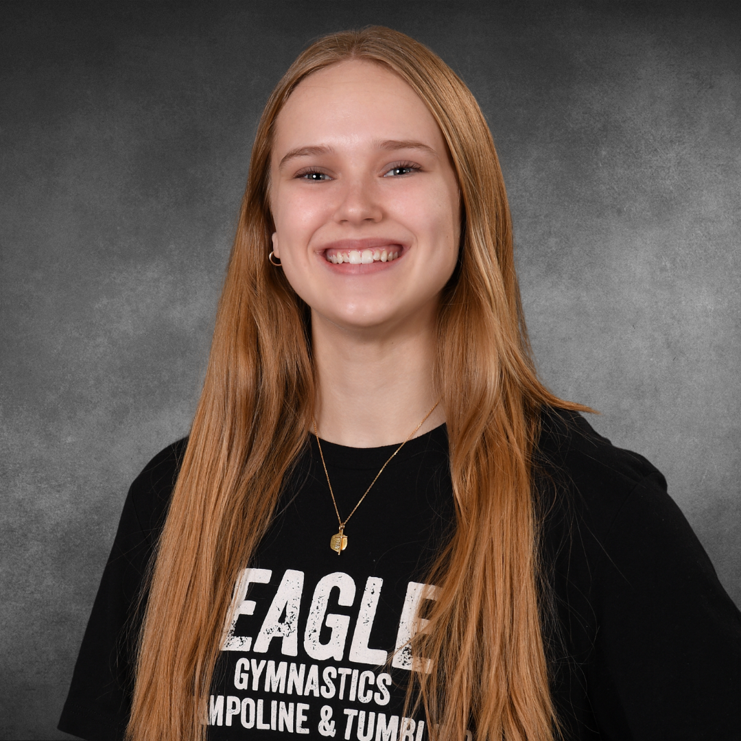 A young woman wearing a black eagle gymnastics t-shirt is smiling for the camera.