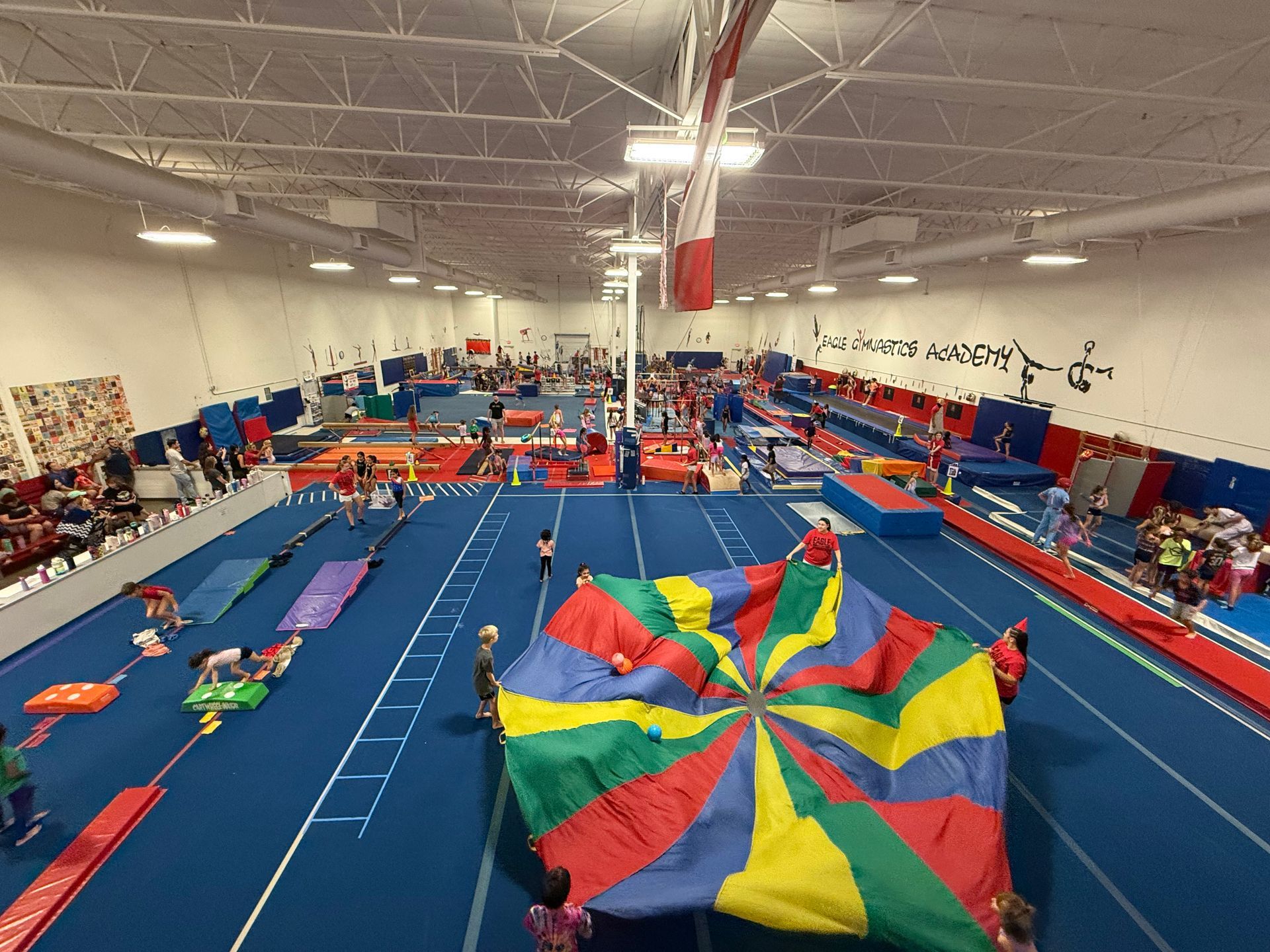 A group of people are playing with a colorful parachute in a gym.