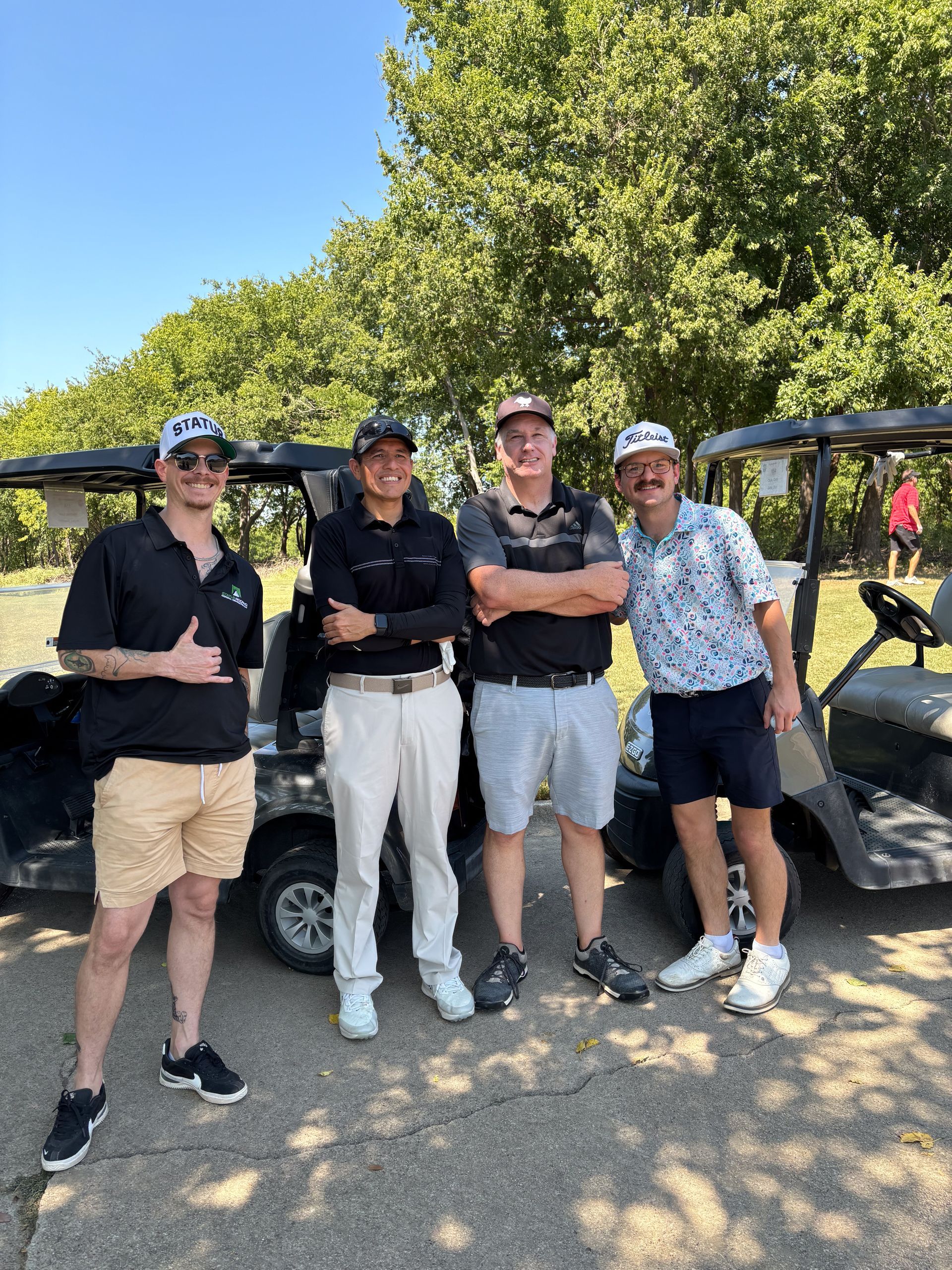 A group of men are standing next to golf carts on a golf course.