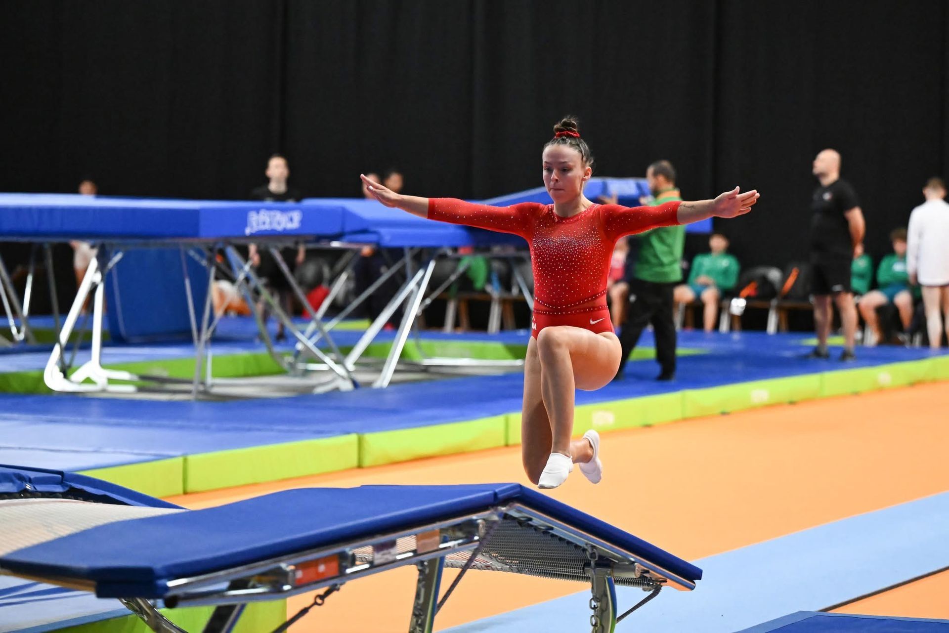 A girl is doing a handstand on a trampoline in a gym.