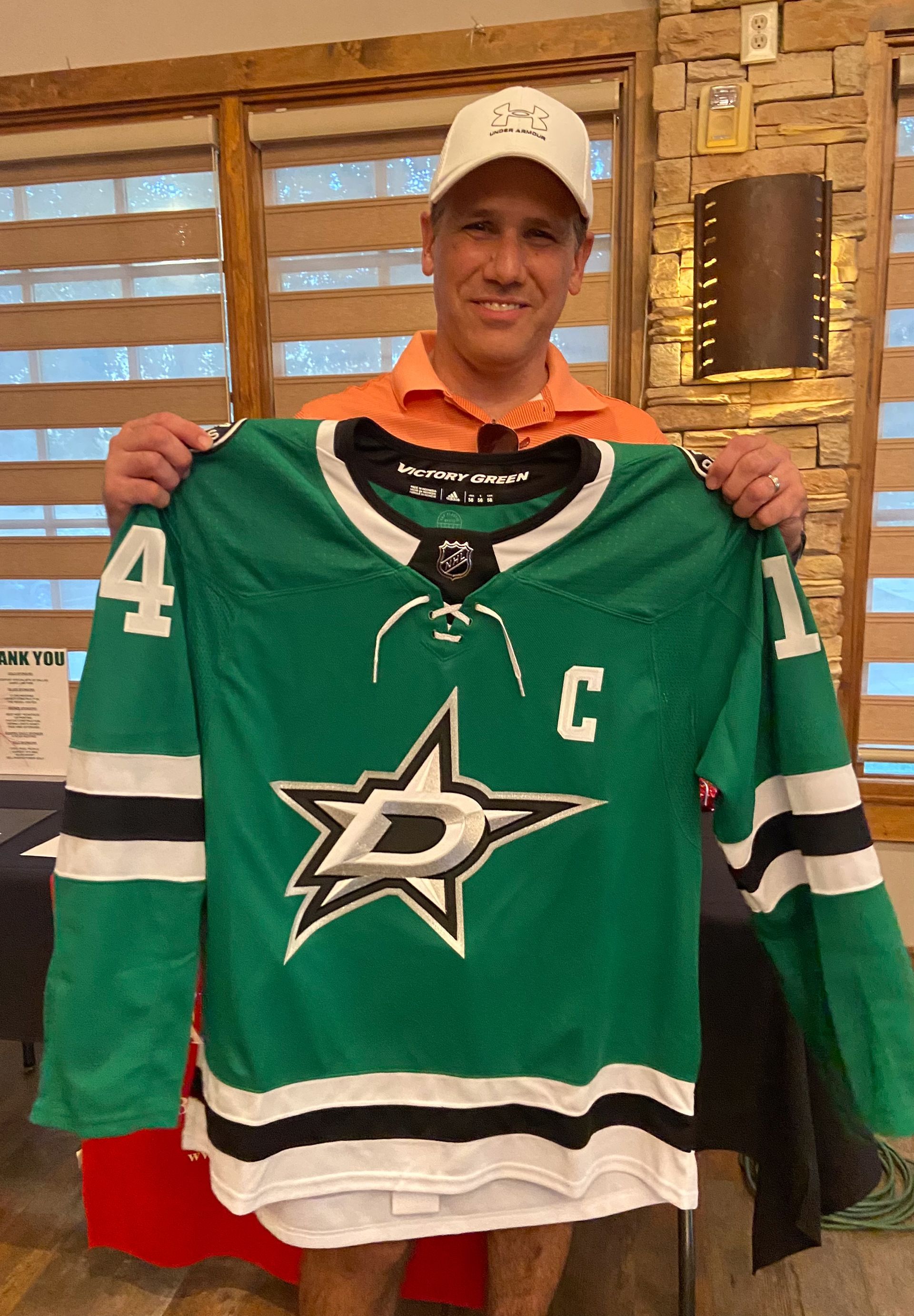 A man is holding a green hockey jersey with a star on it.