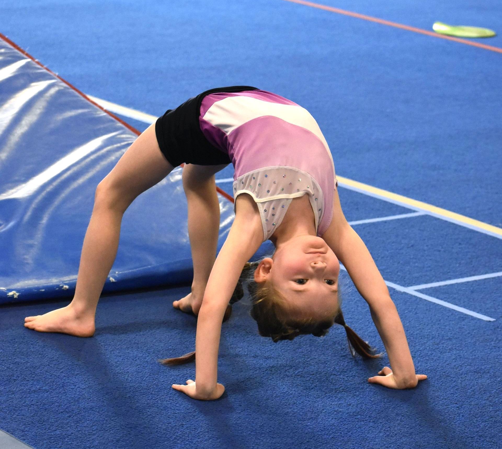 A young girl is doing a handstand on a blue mat