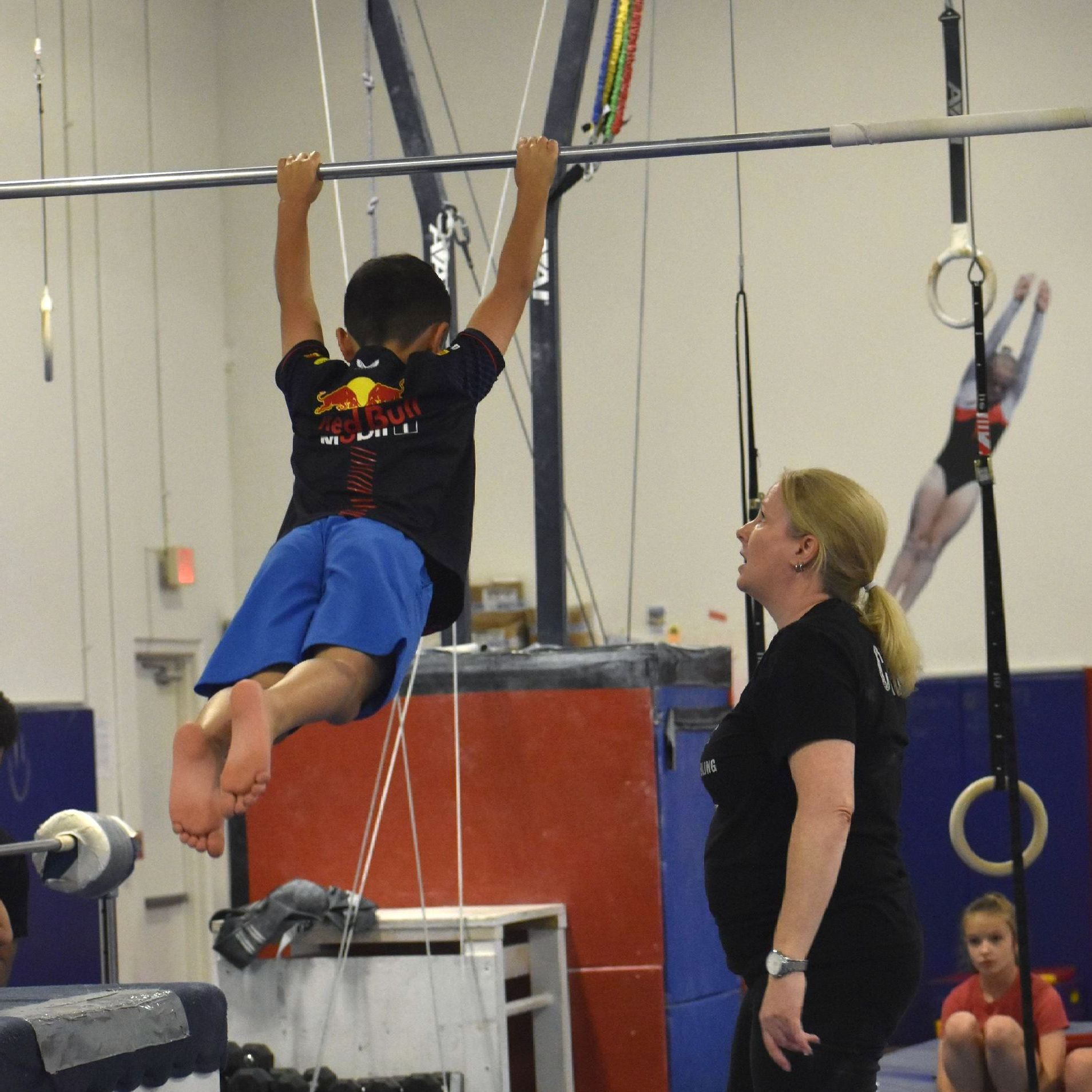 A boy with a red bull shirt on hangs from a bar