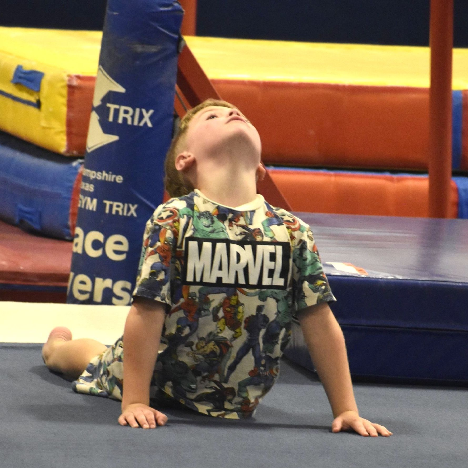 A young boy wearing a marvel shirt is laying on the floor