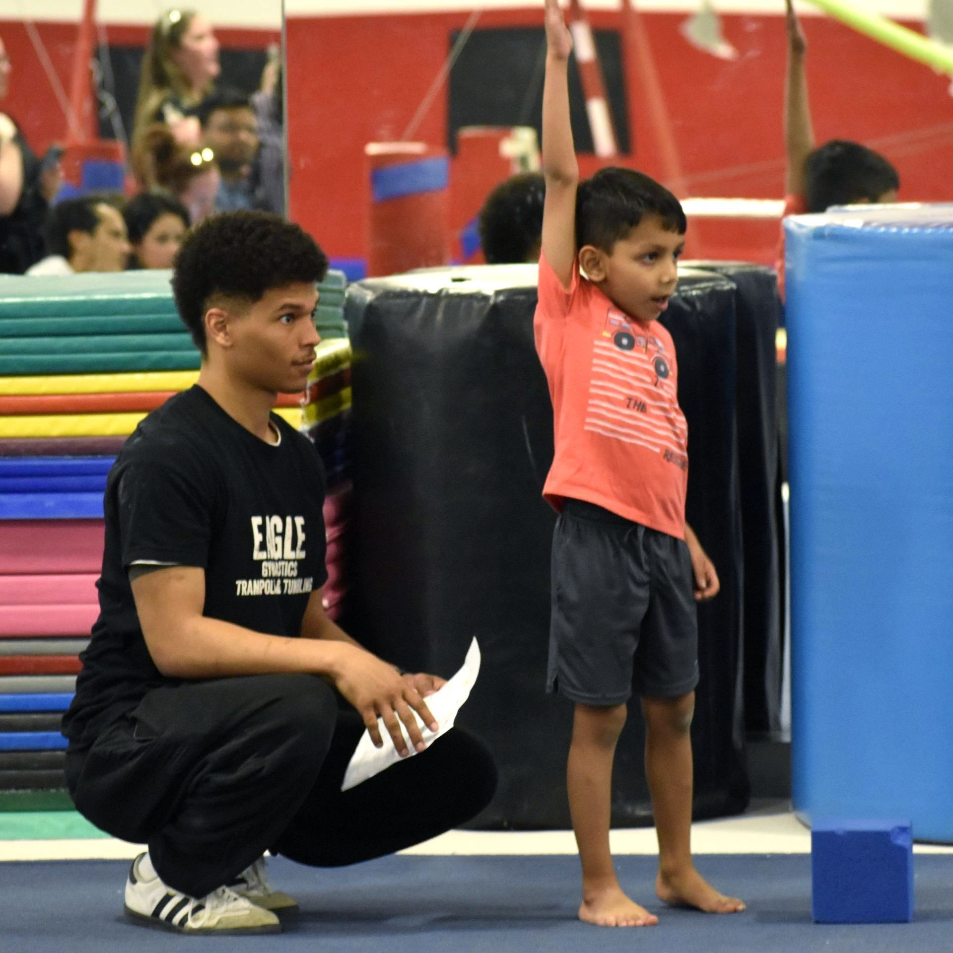 A man squatting next to a young boy wearing a shirt that says eagle