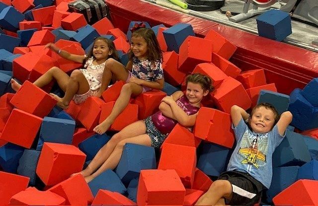 A group of children are sitting in a pile of red and blue foam cubes.