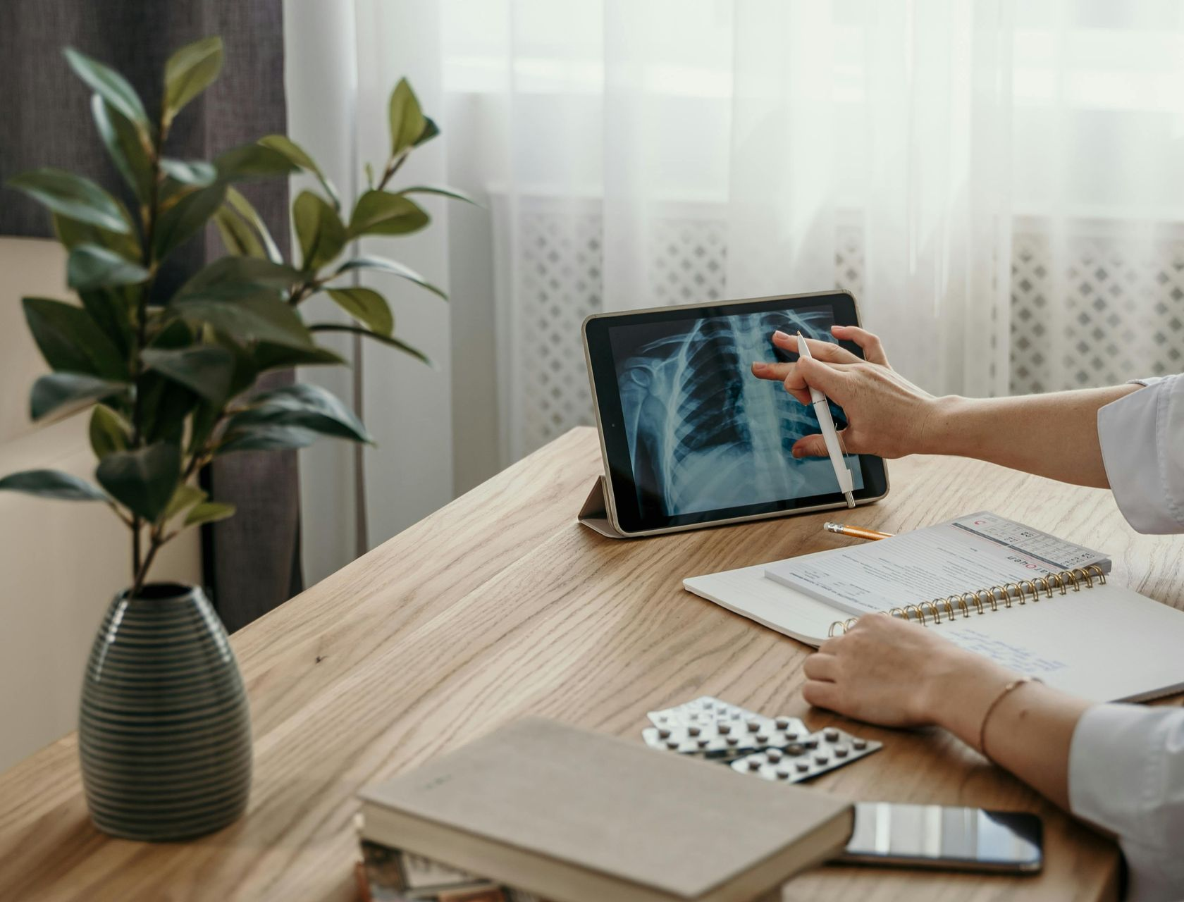 Person using a tablet showing an X-ray at a desk with a plant and notebook