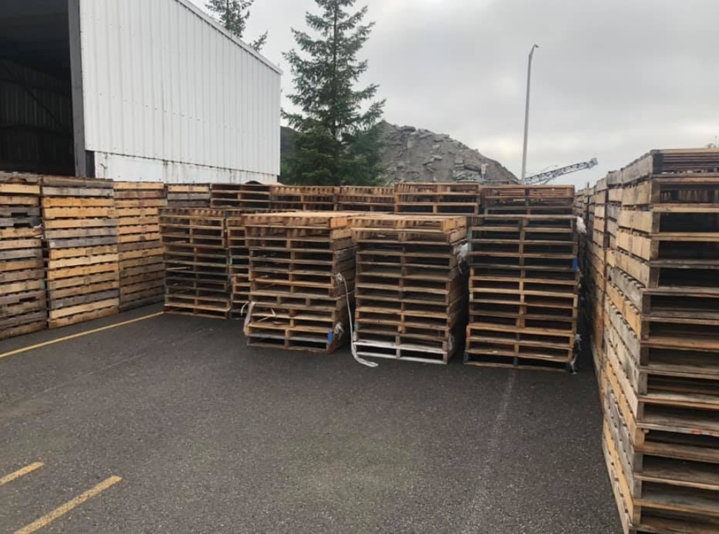 A lot of wooden pallets are stacked on top of each other in a parking lot.