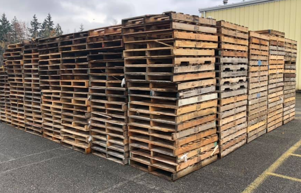 A large pile of wooden pallets are stacked on top of each other in a parking lot.