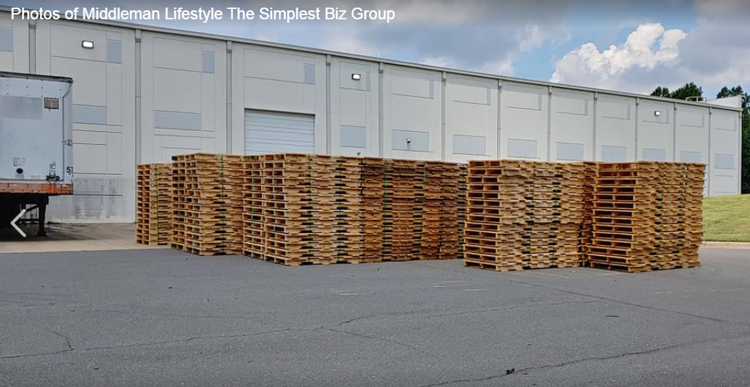 A large stack of wooden pallets in front of a building ready for a student/Pallet recycling
