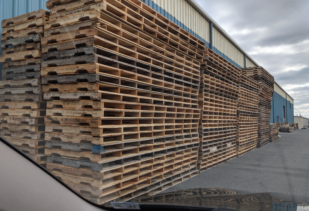 Large stack of wooden pallets in front of a building—explore profitable pallet recycling with The Simplest Biz Training