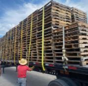A student of the simplest biz is standing next to a truck filled with wooden pallets.