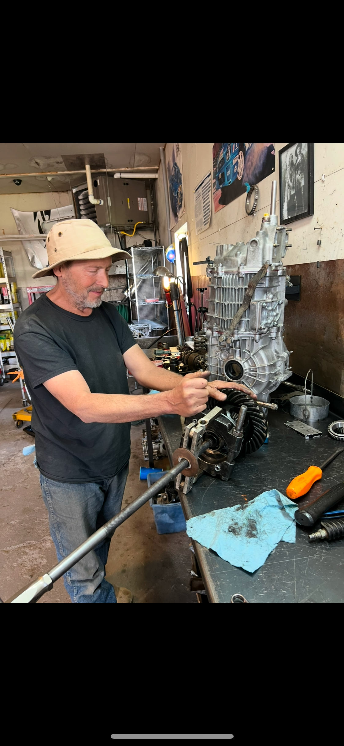 A man in a hat works on a vehicle engine in a cluttered garage.