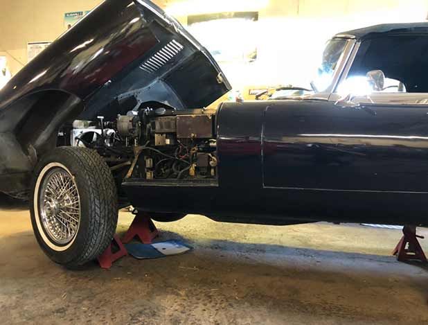 Dark blue classic car, hood open, on jack stands, interior and engine visible.