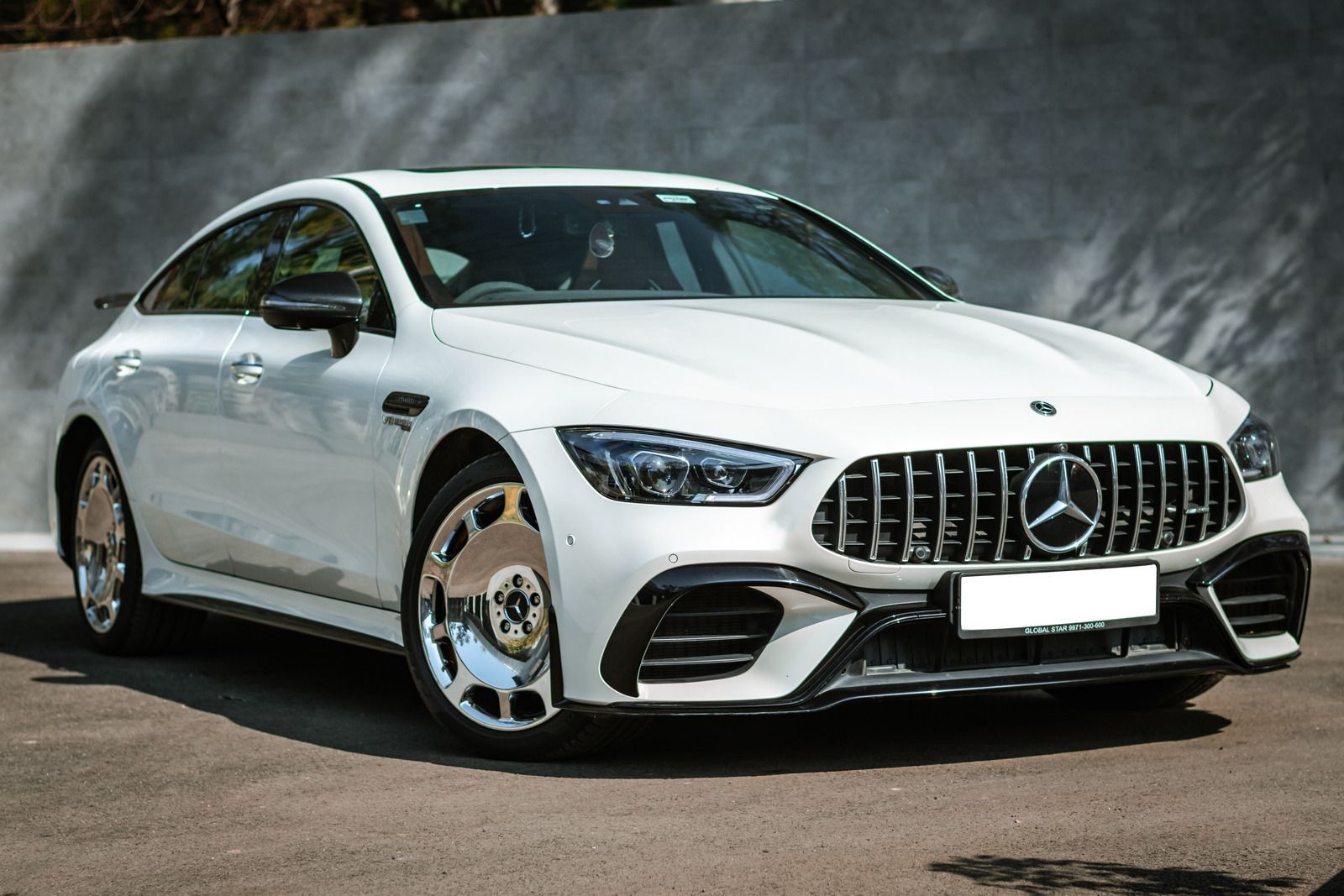 White Mercedes-AMG GT sedan parked in front of a grey wall.