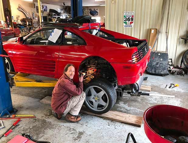 Man welding near the rear wheel of a red Ferrari inside a repair shop.