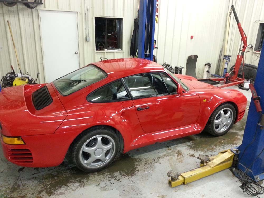 Red Porsche 959 sports car in a garage, with silver wheels and a yellow lift.
