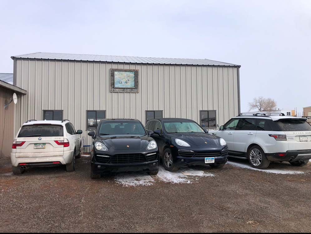 Four SUVs parked in front of a metal building on a snowy day.
