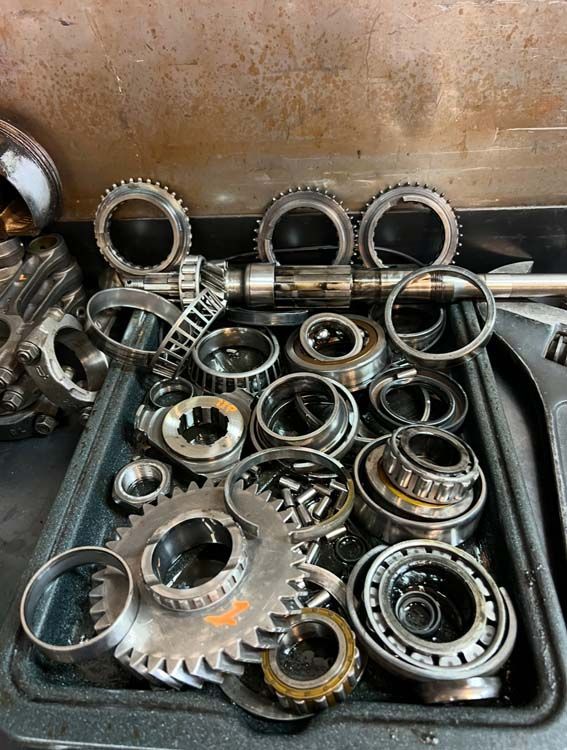 Disassembled transmission components, gears, bearings, and rings, in a parts tray, on a work surface.