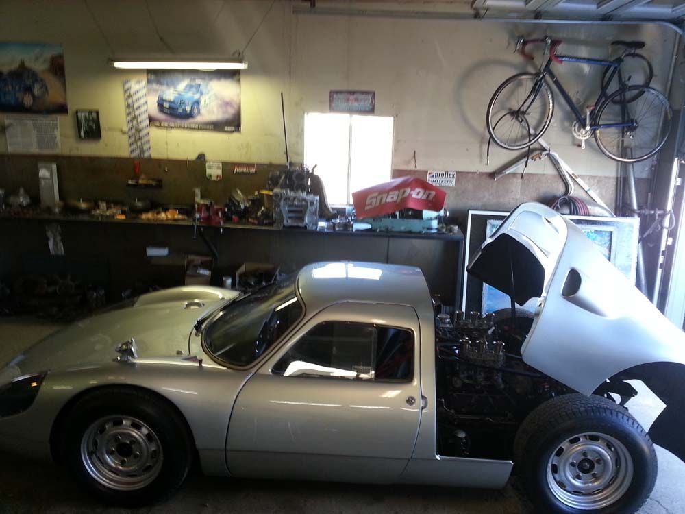Silver sports car in a garage with its hood open, near a bicycle.