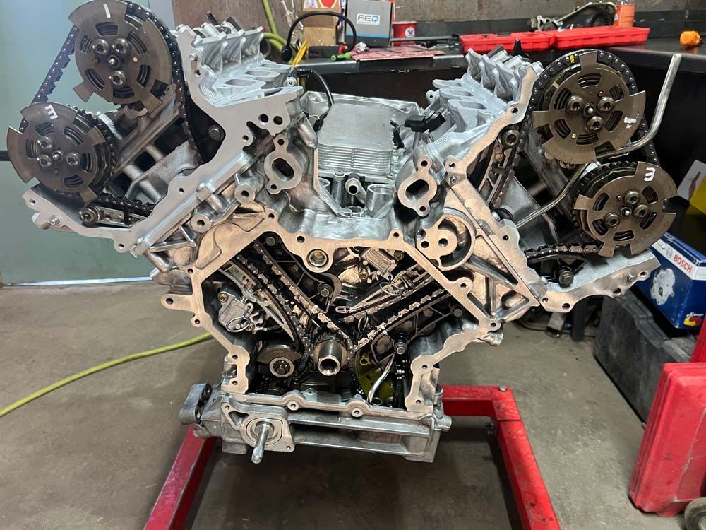 V8 engine on a stand, partially disassembled, with timing chains visible. Silver and gray metal.