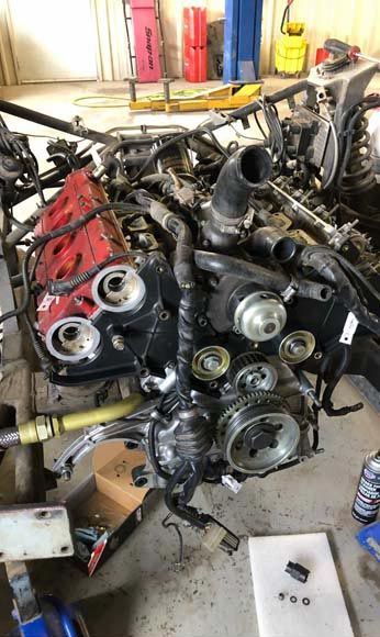 Engine being worked on, with exposed components and red valve covers in a garage.