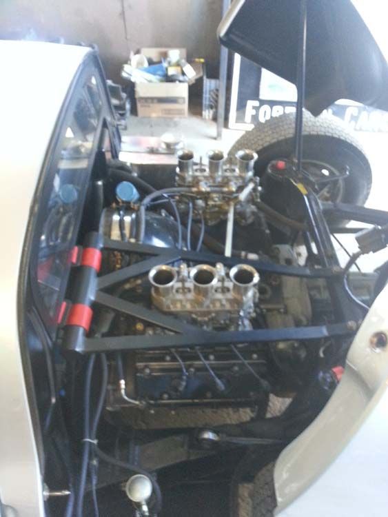 Silver car engine bay with open hood, four carburetors, and black frame.