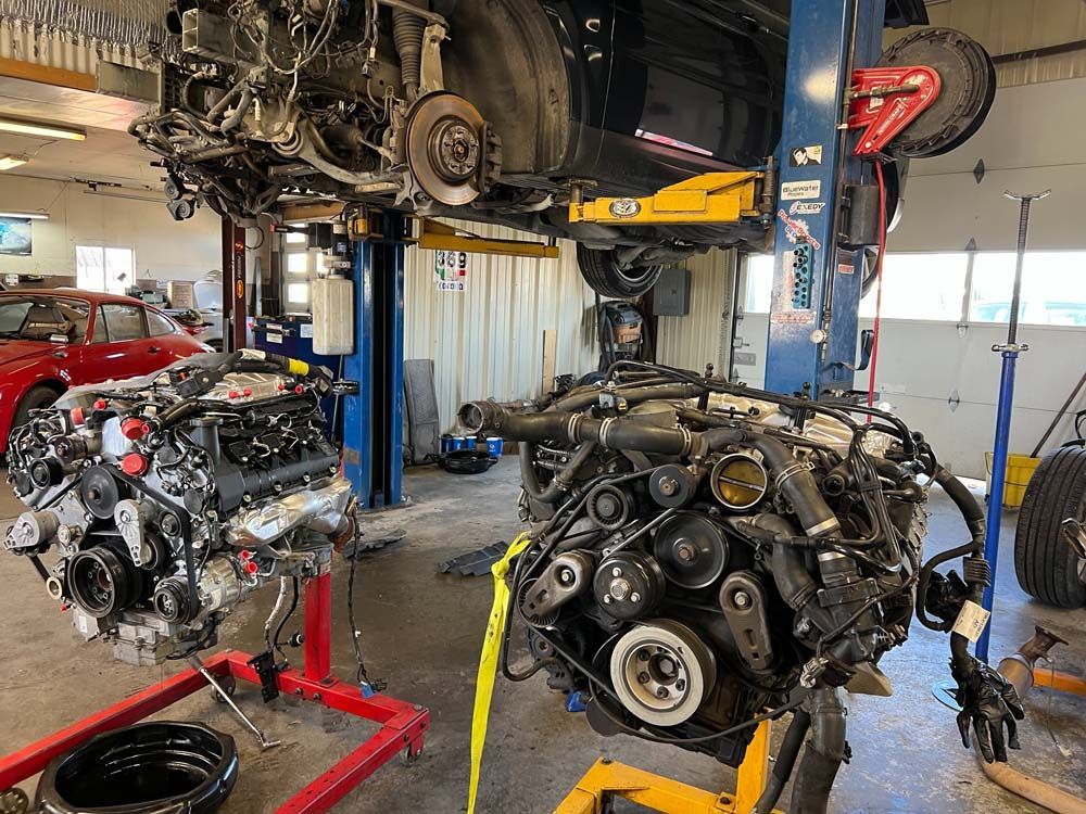 Two car engines on stands in a garage. A car is raised on a lift above them.