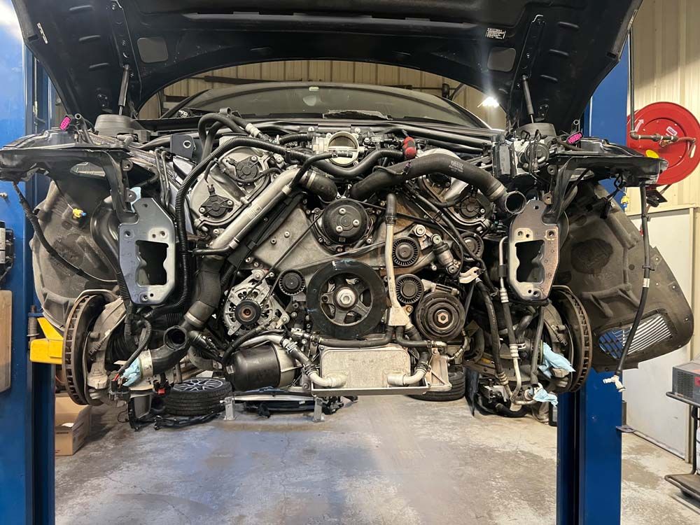 Car engine exposed in a repair shop, elevated on a lift with the hood open.