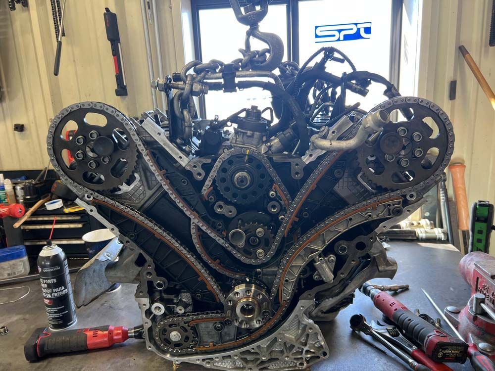 Engine with timing chains exposed, on a workbench, in a garage.