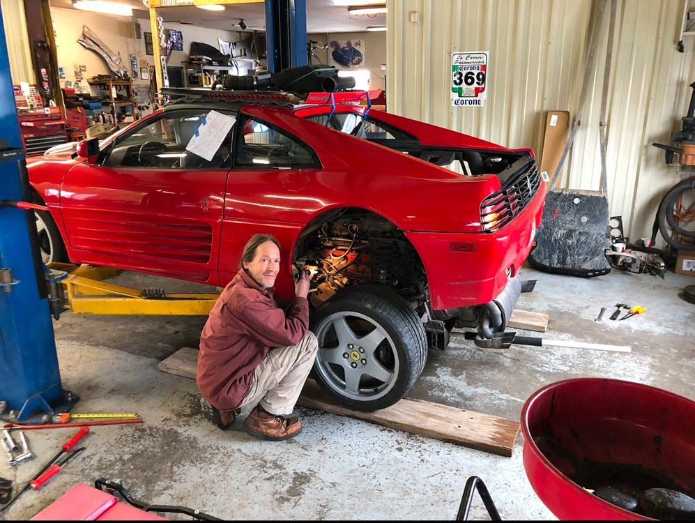 Man working on a red Ferrari in a garage. Car is on a lift.
