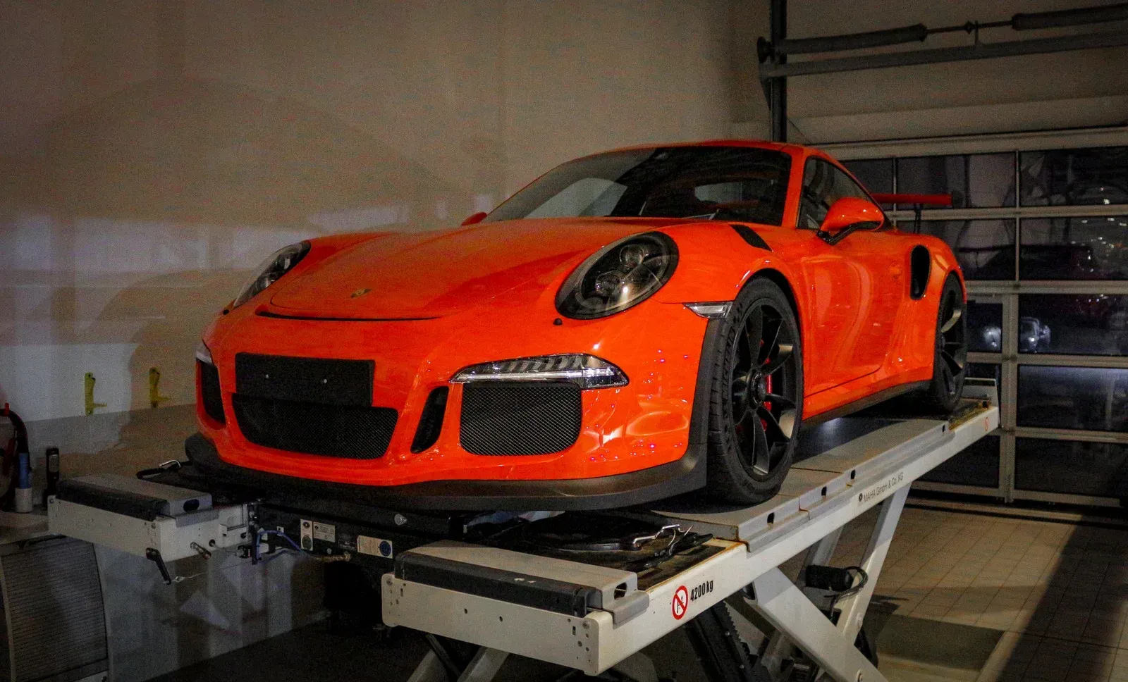 Orange Porsche 911 GT3 RS on a car lift inside a garage.