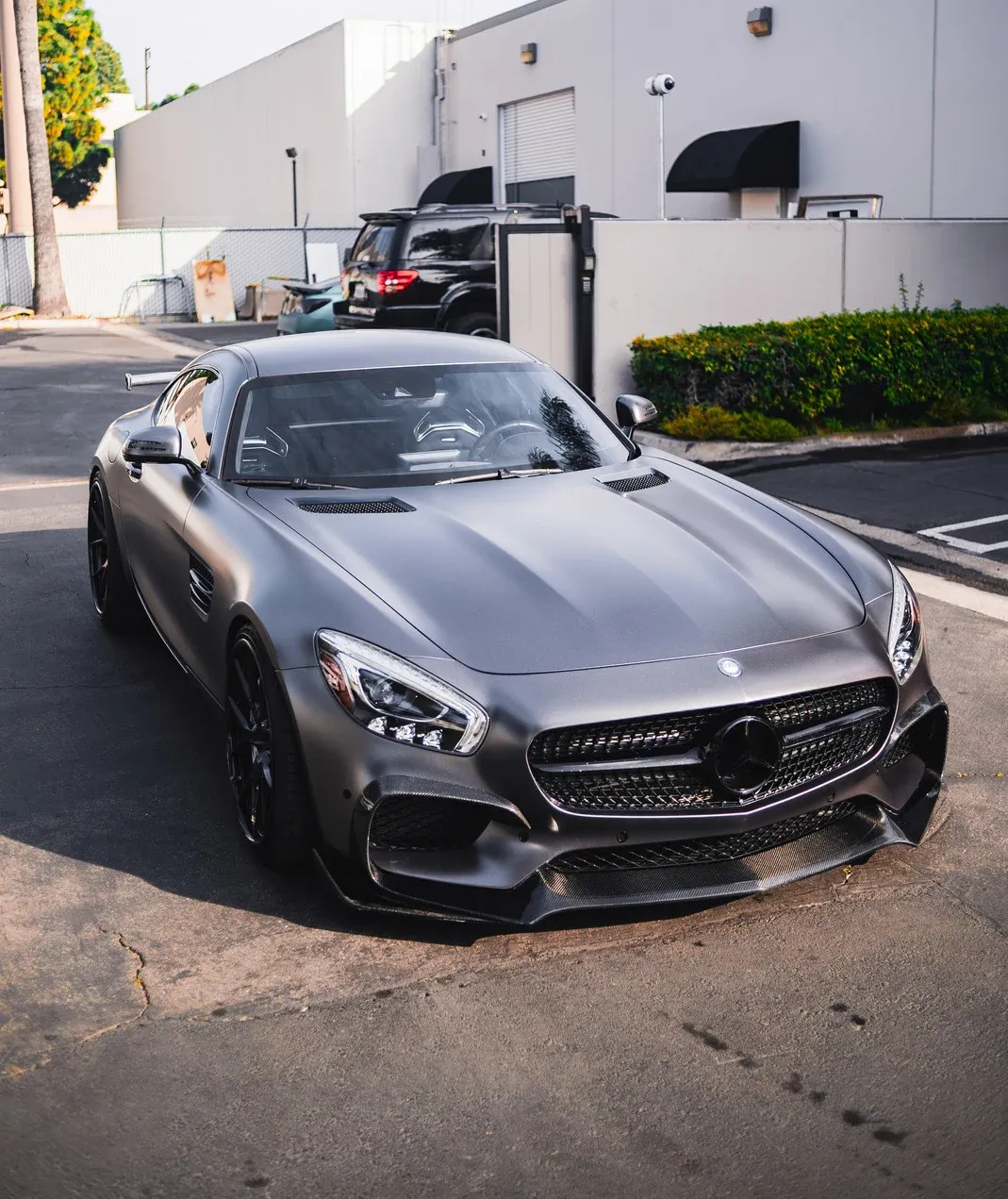Gray Mercedes-AMG GT sports car parked on asphalt in front of a white building.