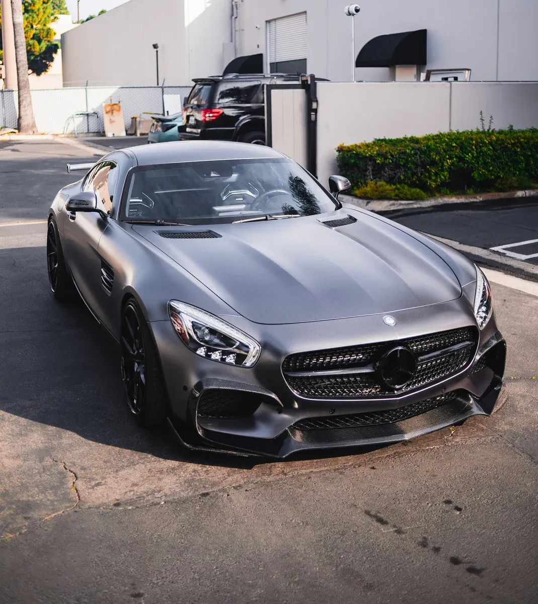Gray Mercedes-AMG GT sports car parked on asphalt, in front of a white building.