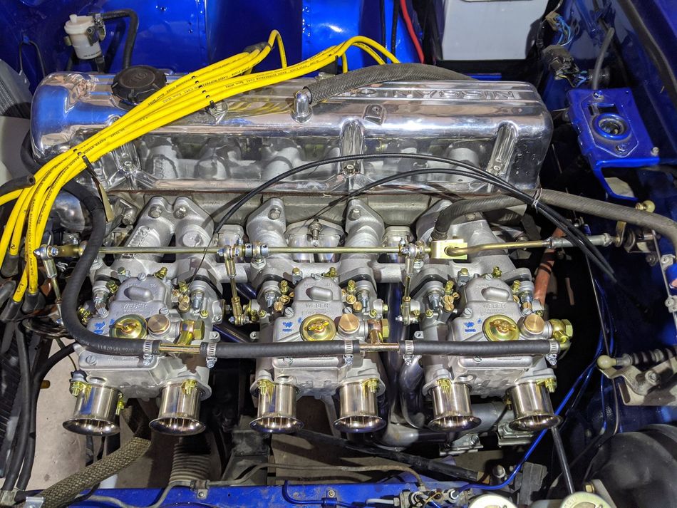 Blue car engine with multiple carburetors, yellow spark plug wires, and chrome accents.