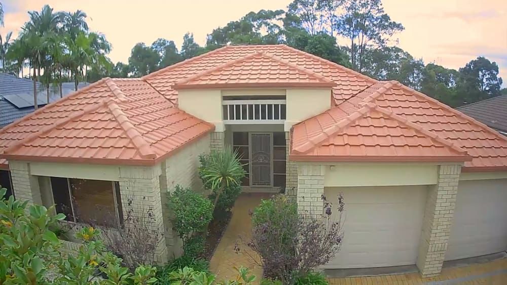 An Aerial View of a House With a Red Tile Roof Surrounded by Trees — Roof Restoration Masters In Watanobbi, NSW